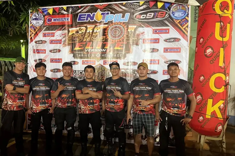 Members of a motorsport team in matching jerseys at a race event backdrop